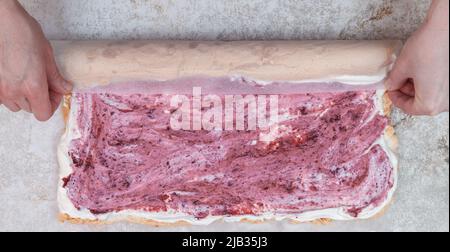 Der Konditor des Küchenchefs rollt die Baiser zu einer Rolle mit Beerenconfit und Creme Stockfoto