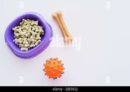 Draufsicht auf knochenförmige Plätzchen in violetter Schale in der Nähe von Gummiball auf weiß isoliert Stockfoto