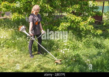 Eine Frau mäht Gras auf seinem Grundstück mit einem Benzintrimmer Stockfoto