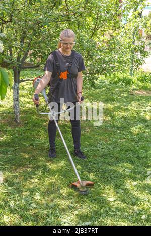 Eine Frau mäht Gras auf seinem Grundstück mit einem Benzintrimmer Stockfoto