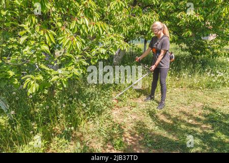 Eine Frau mäht Gras auf seinem Grundstück mit einem Benzintrimmer Stockfoto