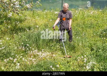 Eine Frau mäht Gras auf seinem Grundstück mit einem Benzintrimmer Stockfoto