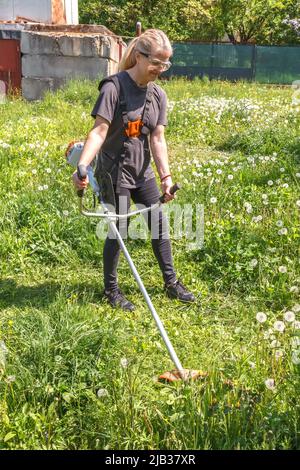 Eine Frau mäht Gras auf seinem Grundstück mit einem Benzintrimmer Stockfoto