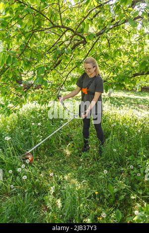 Eine Frau mäht Gras auf seinem Grundstück mit einem Benzintrimmer Stockfoto