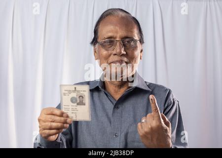 Ein alter indischer Mann lächelt mit Wählerkarte in der Hand auf weißem Hintergrund Stockfoto