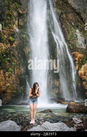 Das kalte, eisige Wasser eines alpinen Wasserfalls unter dem Mount Goverla erfrischt sich nach einem heißen Tag. Gesunde schöne Mädchen badet in schnellen Strömen eines sauberen s Stockfoto