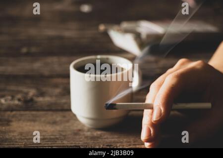 Eine Zigarette in den Händen eines Mädchens auf dem Tisch neben einer Tasse Kaffee, Zigaretten und Kaffee, schlechte Gewohnheiten, Rauchen Stockfoto