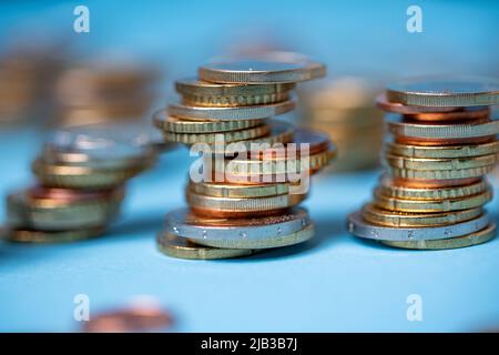 Auf blauem Hintergrund stapelten sich Münzen. Euro-Münzen aus der Europäischen Union. Geld und Bargeld stapelten sich bis zu Türmen Stockfoto