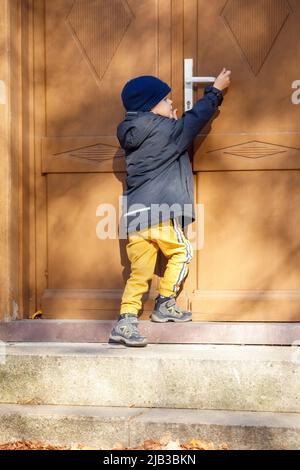 Kleiner Junge versuchen, den Griff der großen braunen Tür zu erreichen. Stockfoto