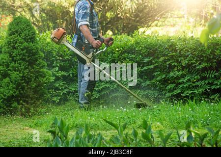 Mann in einem karierten Hemd mit einem manuellen Rasenmäher mäht das Gras im Stadtpark Stockfoto