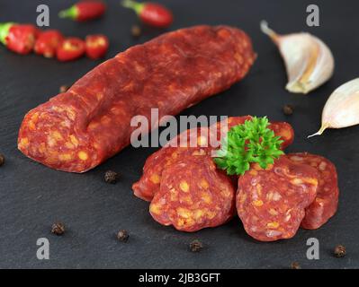 Traditionelle spanische Chorizo-Wurst mit frischen Kräutern, Knoblauch, Pfeffer und Chilischoten, serviert auf schwarzem Schieferbrett, Nahaufnahme. Stockfoto