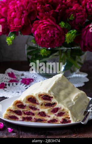 Kuchen Klosterhütte mit Kirschfüllung und saurer Creme, ein Bouquet von Pfingstrosen auf einem Holztisch. Stockfoto