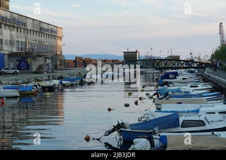 Viele weiße Yachten und private Vergnügungsboote, die in der Marina in der Stadt Koper in der Nähe des Stadtzentrums festgemacht sind. Im Horizont ist Landschaft und Sonnenuntergang Himmel. Stockfoto