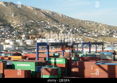 Containerterminal mit verstauten Containern von verschiedenen Spediteuren in Piräus. Dahinter befinden sich Lagertanks für Flüssigkeiten und Wohngebäude. Stockfoto