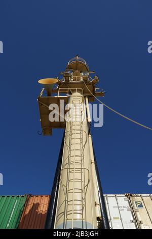 Blick auf den vorderen Schiffsmast mit Leiter und Nebelhorn von der Anlegestelle, von Deck nach oben. Dahinter sind verstaute Container von verschiedenen Spediteuren. Stockfoto