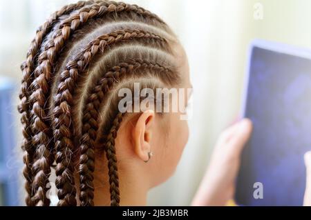 Mädchen mit vielen kleinen Zöpfen, die die Tablette vor sich halten. Nahaufnahme, selektiver Fokus Stockfoto