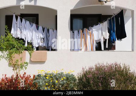Wäsche hängt auf einem Balkon Wäscheleine auf weißen Hauswand Hintergrund. Tun Hausarbeiten Lifestyle und Haushaltsreinigung Konzept Stockfoto