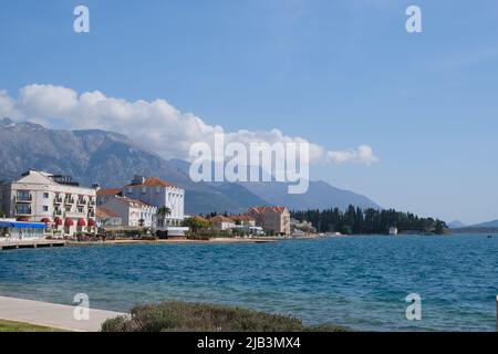 Häuser am Ufer der bucht von kotor, Tivat, Montenegro. Wolken über Bergen in blauem Himmel um Stadt, Wald und Seehafen. Wunderschöne Naturlandschaft Stockfoto