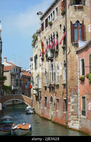 Venedig, Italien. Blick auf einen Kanal mit einer kleinen Brücke, flankiert von historischen Gebäuden. Einige Boote sind im Wasser sichtbar Stockfoto