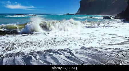 Wunderschöne abgeschiedene schwarze Lavasandstrandbucht, Felsen, große, starke, plätschernden Wellen, blauer Himmel - Caleta playa Hermigua, La Gomera Stockfoto