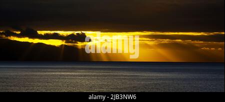 Schöner atmosphärischer Himmel, gelborangener Sonnenuntergang über dem ruhigen atlantischen Ozean, Sonne bricht durch Stratocumulus Sturmwolken, Sonnenstrahlen - Cana Stockfoto
