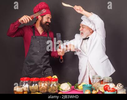 Zwei Köche in Uniform kämpfen mit Küchenutensilien. Kochen. Kulinarischer Kampf. Wettbewerb des Küchenchefs. Stockfoto