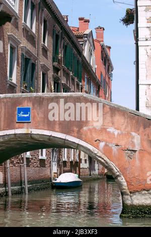 Romantischer Blick auf die enge Straße von Venedig mit alten Gebäuden und Brücke über einem Kanal. Boot schweben auf dem Wasser, sonniger Tag blauer Himmel. Italienische Feiertage. Stockfoto