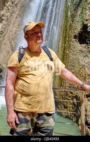 Ein Mann steht vor einem Wasserfall. Herbstwasserstrom Ayun. Fluss Nahal Ayun. Reserve und Nationalpark. Oberes Galiläas, Israel. Nahaufnahme. Stockfoto