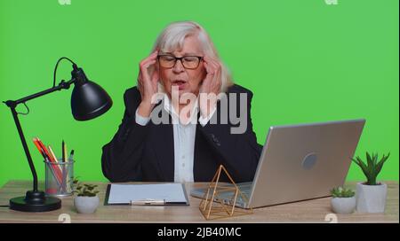 Unzufrieden Senior Geschäftsfrau reiben Schläfen, um Kopfschmerzen Problem zu heilen, leiden unter Spannung und Migräne, Stress, Grimacing bei Schmerzen Bluthochdruck im Büro. Ältere Frau grün Chroma-Taste Stockfoto