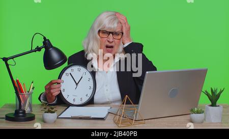 Leitende Geschäftsfrau mit Angst, die Zeit auf der Uhr zu überprüfen, zu spät zur Arbeit zu laufen, im Büro zu spät dran zu sein. Ältere Frau, die Stunden und Minuten betrachtet und sich Sorgen macht, pünktlich auf dem Chroma Key Studio zu sein Stockfoto