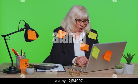 Müde erschöpft Müdigkeit Senior Business Frau Büroangestellte Manager sitzt im Bürotisch mit Laptop Haftnotizen Sticks mit vielen Aufgaben Beschriftung helfen, fühlt sich traurig Langeweile überarbeitetes Multitasking Stockfoto