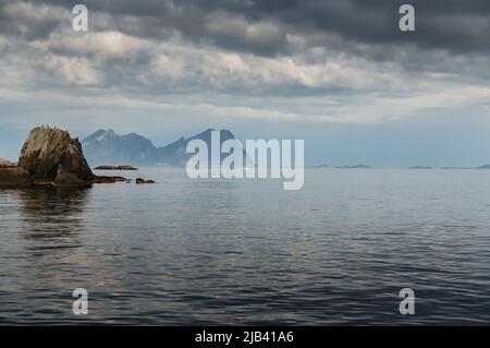 Segelyacht am Horizont, norwegische Küste, felsige Küste mit dramatischem Himmel, die Sonne bricht durch die Wolken, schiere Klippen, kleine Inseln Stockfoto