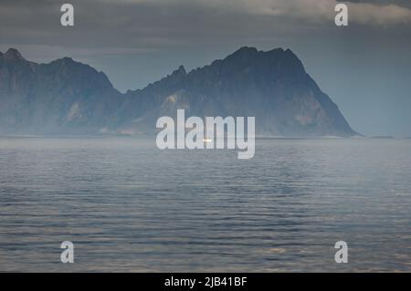 Segelyacht am Horizont, norwegische Küste, felsige Küste mit dramatischem Himmel, die Sonne bricht durch die Wolken, schiere Klippen, kleine Inseln Stockfoto