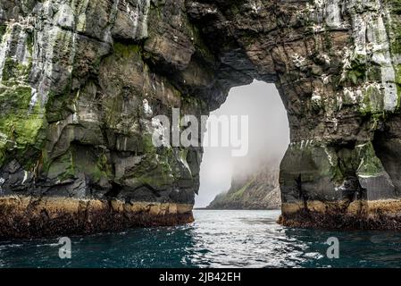 Die Insel Tindhólmur wird durch den Bogen der Gesteinsformation Stori Drangur von Drangarnir auf Vagar, Färöer Inseln, gesehen Stockfoto