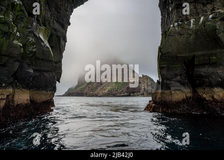 Die Insel Tindhólmur wird durch den Bogen der Gesteinsformation Stori Drangur von Drangarnir auf Vagar, Färöer Inseln, gesehen Stockfoto