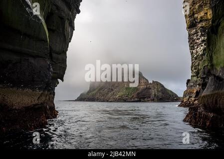 Die Insel Tindhólmur wird durch den Bogen der Gesteinsformation Stori Drangur von Drangarnir auf Vagar, Färöer Inseln, gesehen Stockfoto