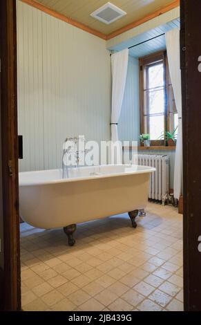 Weiße freistehende, rollstuhlgerechte Badewanne mit Füßen im Badezimmer im alten, ca. 1832 Jahre alten, im kanadischen Cottage-Stil gehaltenen Feldsteinhaus. Stockfoto
