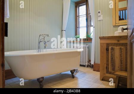 Weiße freistehende, rollstuhlgerechte Badewanne mit Füßen im Badezimmer im alten, ca. 1832 Jahre alten, im kanadischen Cottage-Stil gehaltenen Feldsteinhaus. Stockfoto