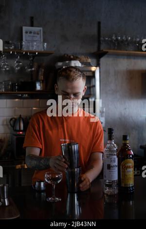Der Barkeeper macht im Nachtclub einen Cocktail. Ein junger Mann mischt einen Cocktail in einem dunklen Loft-Café. Ein Alkoholgetränk in der modernen Bar. Ein Barkeeper. Stockfoto