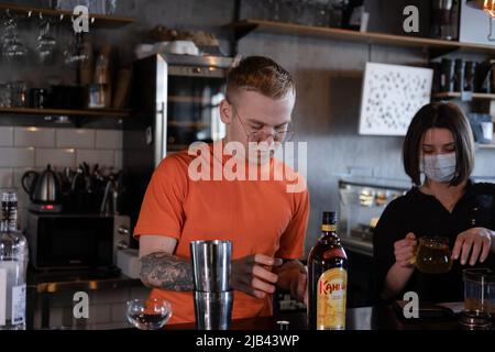 Der Barkeeper macht im Nachtclub einen Cocktail. Ein junger Mann mischt einen Cocktail in einem dunklen Loft-Café. Ein Alkoholgetränk in der modernen Bar. Ein Barkeeper. Stockfoto