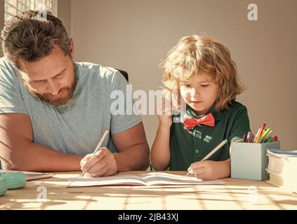 Bärtiger Vater schreibt Schulaufgaben mit seinem Sohn im Klassenzimmer, Bildung Stockfoto