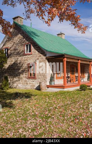 Altes, um 1850 im kanadischen Cottage-Stil geschnittenes Steinhaus mit grünem Blechdach im Herbst. Stockfoto