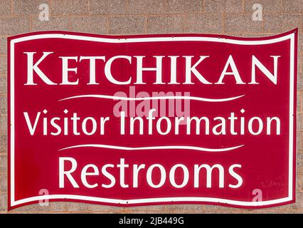 Ketchikan, Alaska, USA - 17. Juli 2011: Nahaufnahme eines weißen Schildes auf dem roten Stadtschild, das das Besucherzentrum und die Toilette im Hafen benennt. Stockfoto