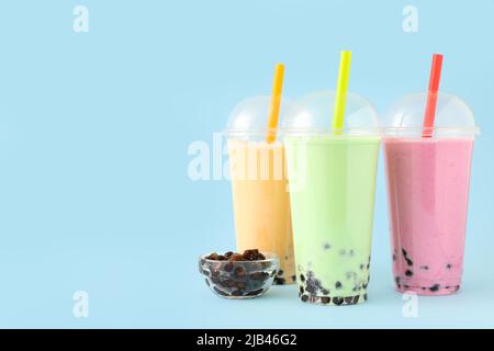 Plastikbecher mit verschiedenen leckeren Bubble Tea auf blauem Hintergrund Stockfoto