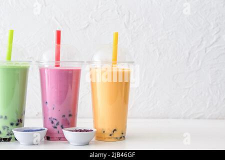 Plastikbecher mit verschiedenen leckeren Bubble Tee und Pulver auf dem Tisch Stockfoto
