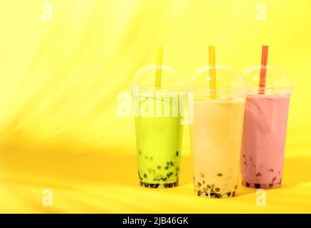 Plastikbecher mit verschiedenen leckeren Bubble Tea auf gelbem Hintergrund Stockfoto