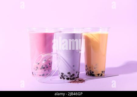 Plastikbecher mit verschiedenen leckeren Blase Tee auf lila Hintergrund Stockfoto