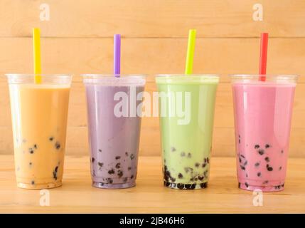 Plastikbecher mit verschiedenen leckeren Bubble Tea auf Holzhintergrund Stockfoto
