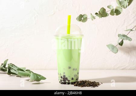 Plastikbecher mit leckeren Bubble Tea und Eukalyptuszweigen auf weißem Hintergrund Stockfoto
