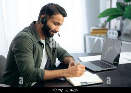 Online-Handel und Börsenkonzept. Ein indischer oder arabischer Mann, der sich vor dem Kauf auf den Aktienkurs auf dem Online-Marktplatz konzentriert, nutzt einen Laptop, während er in seinem modernen Büro sitzt Stockfoto